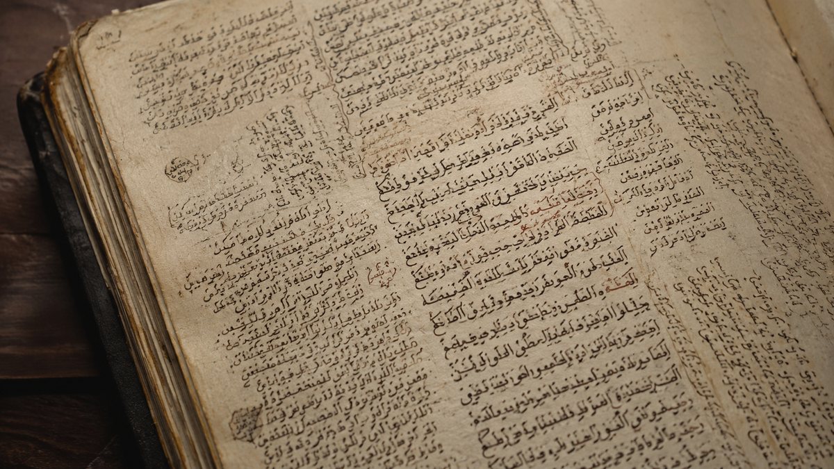 Aufgeschlagene Seite einer alten arabischen Handschrift mit dicht beschriebenen Spalten und Randkommentaren